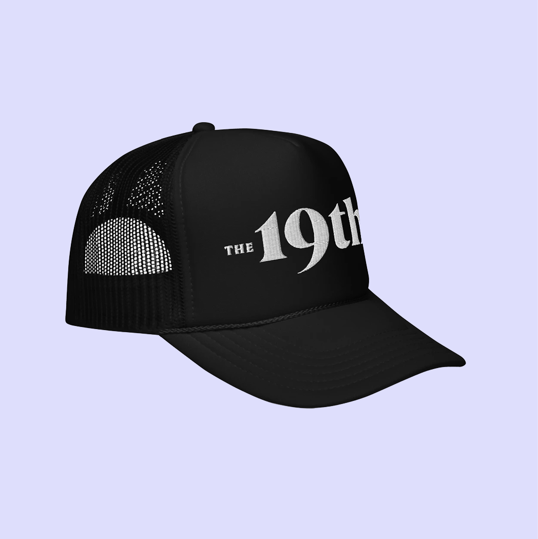 A black trucker-style cap with white text reading 'The 19th*' on the front, shown against a light lavender background, tilted.