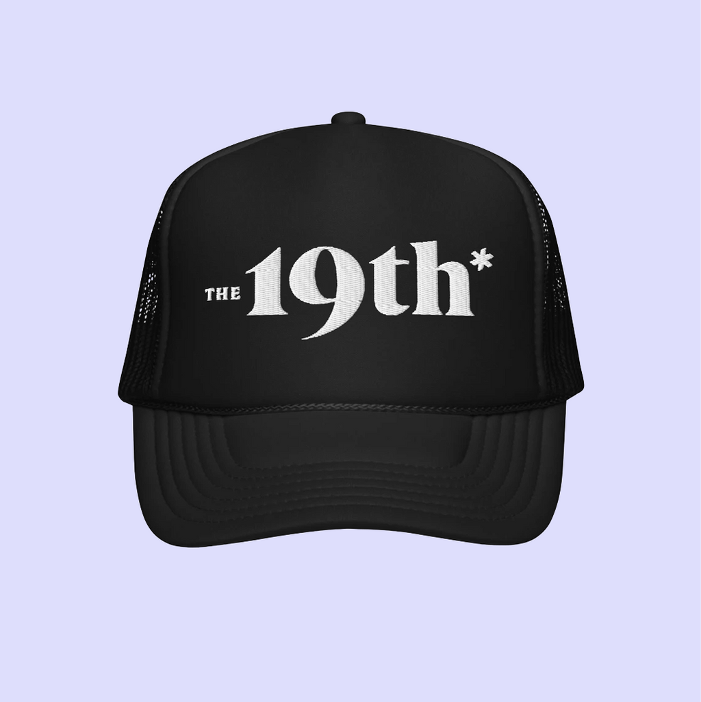A black trucker-style cap with white text reading 'The 19th*' on the front, shown against a light lavender background.