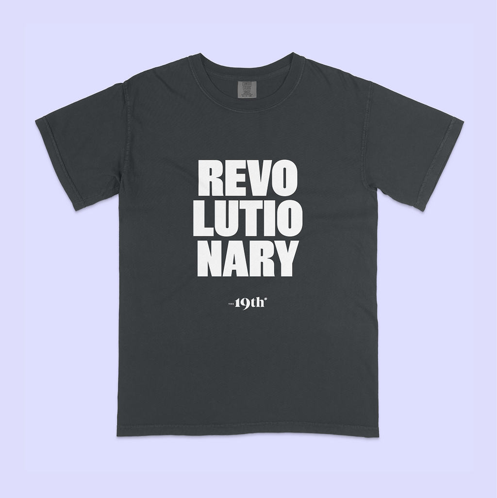 A dark charcoal gray t-shirt with bold white text reading 'REVOLUTIONARY' and smaller text below reading '19th', displayed flat against a light lavender background.