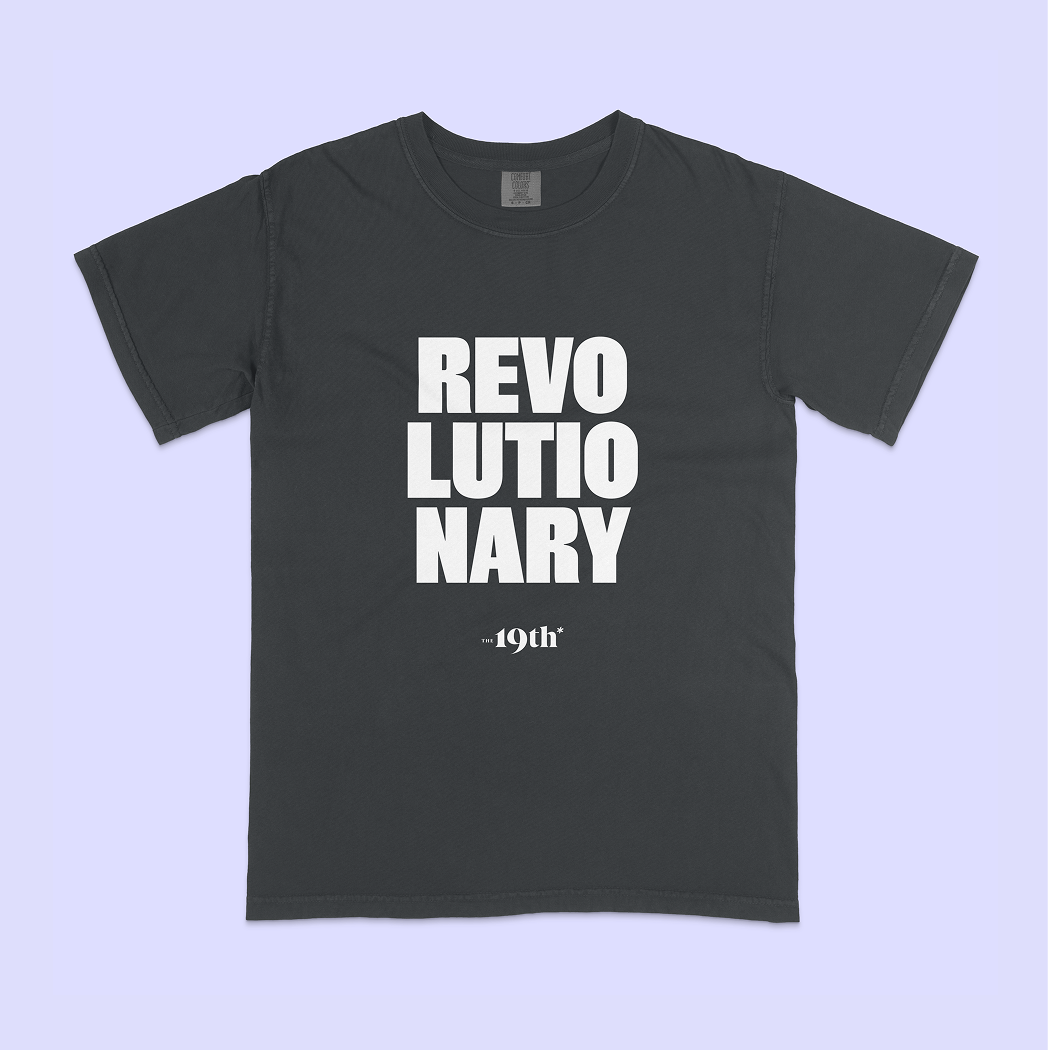 A dark charcoal gray t-shirt with bold white text reading 'REVOLUTIONARY' and smaller text below reading '19th', displayed flat against a light lavender background.